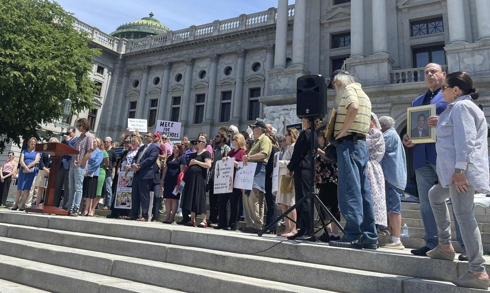 Caleb Kauffman, at podium, speaks at a rally outside of the Pennsylvania state Capitol in Harrisburg, Pa., June 5, 2023. Kauffman, a survivor and advocate, and others were calling on the state Senate to pass two pieces of legislation that would open a two-year window for child sex abuse survivors to file otherwise outdated lawsuits over their claim. (AP Photo/Brooke Schultz)